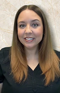 Dental assistant Lauren with ombre brown hair in black scrubs smiling against marble wall.