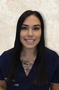 Smith Orthodontics assistant Sabrina in navy scrubs, visible tattoos, smiling against textured marble wall.